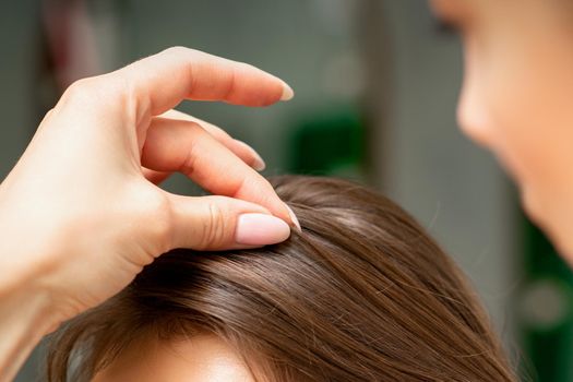 A hairdresser is making the hairstyle of a young brunette woman in a hair salon, close up