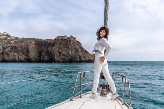 Woman standing on the nose of the yacht at a sunny summer day, breeze developing hair, beautiful sea on background.