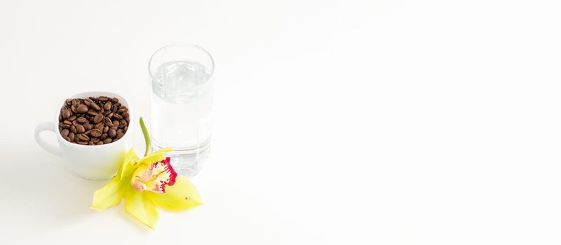 Cup of coffee beans and glass of water with yellow orchid flower against a white background