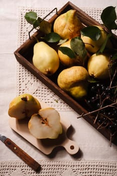 Ripe yellow pears and chokeberry in brown wooden box, prepared for jam cooking on rustical tablecloth, top view, flat lay.