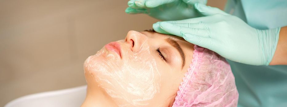 Face peeling at the beautician. Facial treatment. The beautician applies a cleansing face mask to the female patient