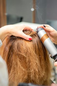 Hands of female hairstylist curls hair client with a curling iron in a hairdressing salon, close up