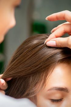 A hairdresser is making the hairstyle of a young brunette woman in a hair salon, close up