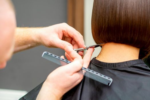 The hairdresser cuts the hair of a brunette woman. Hairstylist is cutting the hair of female client in a professional hair salon, close up