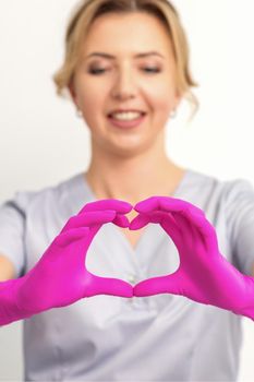 A smiling caucasian woman doctor wearing pink gloves in uniform showing the symbol of a heart against a white background