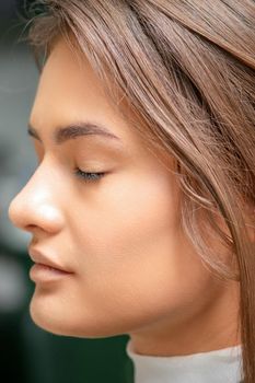 Portrait of a sensual young caucasian woman with closed eyes showing makeup tan on her face and hairstyle in a beauty salon