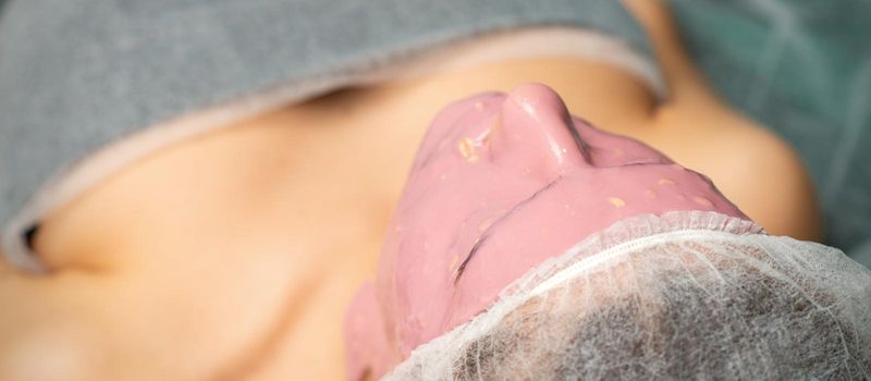 Women skin beauty treatment care. Young woman with alginate cosmetic pink mask on facial skin in beauty spa salon