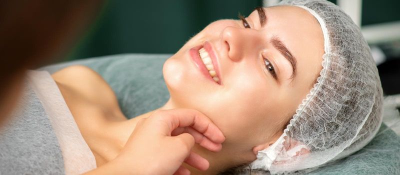 Plastic surgery and beauty concept. Hand of beautician examining and touching the face of beautiful young smiling caucasian woman