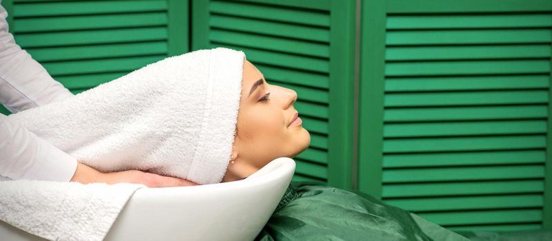 Hairdresser wraps hair of a young caucasian woman in a white towel after washing head in the hairdressing salon