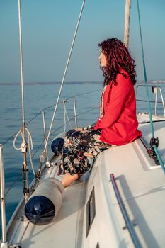 A woman sits on the bow of a yacht on a sunny summer day, the breeze develops her hair, a beautiful sea is in the background.