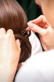 A hairdresser is making the hairstyle of a young brunette woman in a hair salon, close up