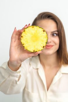 A young attractive pretty nice caucasian smiling woman holds ring slice pineapple covering her eye against a white background. Healthy eating concept