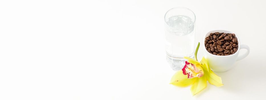 Cup of coffee beans and glass of water with yellow orchid flower against a white background