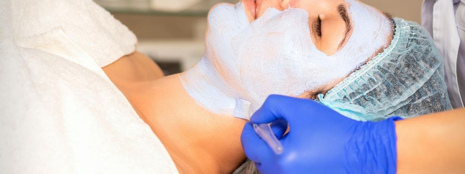 Face peeling at the beautician. Facial treatment. The beautician applies a cleansing face mask to the female patient