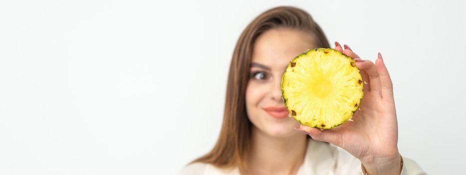 A young attractive pretty nice caucasian smiling woman holds ring slice pineapple covering her eye against a white background. Healthy eating concept
