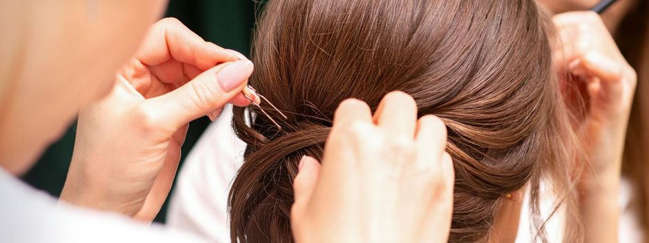 A hairdresser is making the hairstyle of a young brunette woman in a hair salon, close up