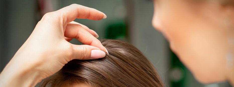 A hairdresser is making the hairstyle of a young brunette woman in a hair salon, close up