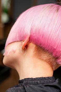 Styling and cutting dyed pink hair of young model back view in a hairdressing salon. Pink short hairstyle