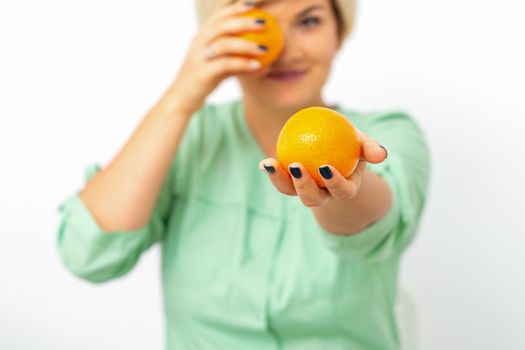 Smiling female nutritionist holding a whole orange, offering and looking at camera over white background, healthy diet concept