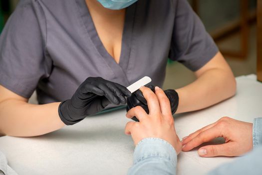 Close up of the caucasian hands of a professional manicurist are filing the nails of a young woman. Young caucasian woman receiving a manicure by a beautician with a nail file in a nail salon