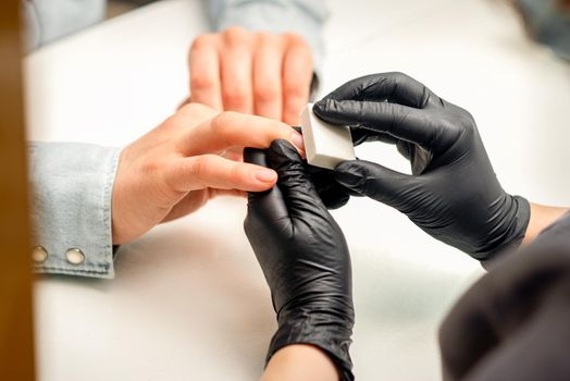 Close up of the caucasian hands of a professional manicurist are filing the nails of a young woman. Young caucasian woman receiving a manicure by a beautician with a nail file in a nail salon