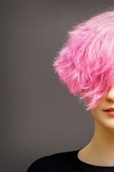 Beautiful young caucasian woman with short curly bob hairstyle dyed in pink color with closed eyes against dark gray background with copy space