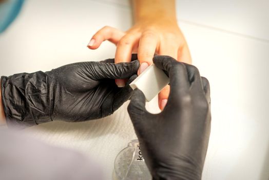 Close up of the caucasian hands of a professional manicurist are filing the nails of a young woman. Young caucasian woman receiving a manicure by a beautician with a nail file in a nail salon