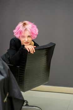 Portrait of a beautiful young caucasian woman with a new short pink hairstyle sitting in a chair at a hairdresser salon