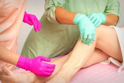 Waxing depilation procedure for removing hair on legs with sugaring paste in the beauty salon