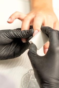 Close up of the caucasian hands of a professional manicurist are filing the nails of a young woman. Young caucasian woman receiving a manicure by a beautician with a nail file in a nail salon