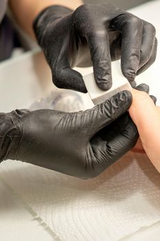 Close up of the caucasian hands of a professional manicurist are filing the nails of a young woman. Young caucasian woman receiving a manicure by a beautician with a nail file in a nail salon