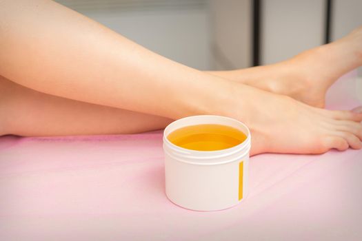 Woman legs with a white jar of wax sugaring before hair removal at the spa