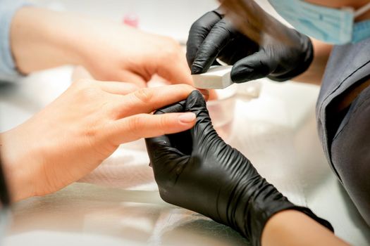 Close up of the caucasian hands of a professional manicurist are filing the nails of a young woman. Young caucasian woman receiving a manicure by a beautician with a nail file in a nail salon