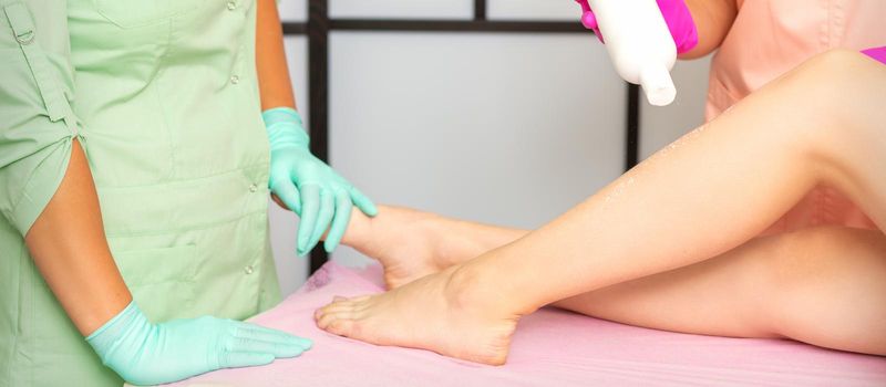 Procedure sugaring. A cosmetologist is sprinkling talcum powder on a young female leg before the depilation procedure