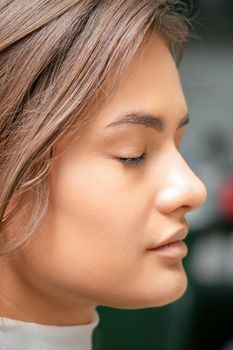 Portrait of a sensual young caucasian woman with closed eyes showing makeup tan on her face and hairstyle in a beauty salon