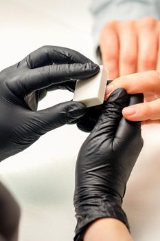 Close up of the caucasian hands of a professional manicurist are filing the nails of a young woman. Young caucasian woman receiving a manicure by a beautician with a nail file in a nail salon