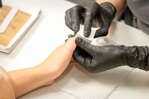 Close up of the caucasian hands of a professional manicurist are filing the nails of a young woman. Young caucasian woman receiving a manicure by a beautician with a nail file in a nail salon