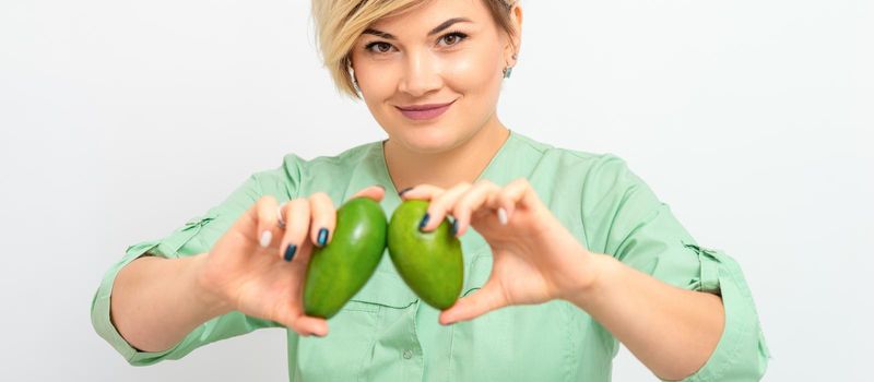 Female nutritionist doctor wearing green workwear holding green organic avocado fruit. Healthy lifestyle concept