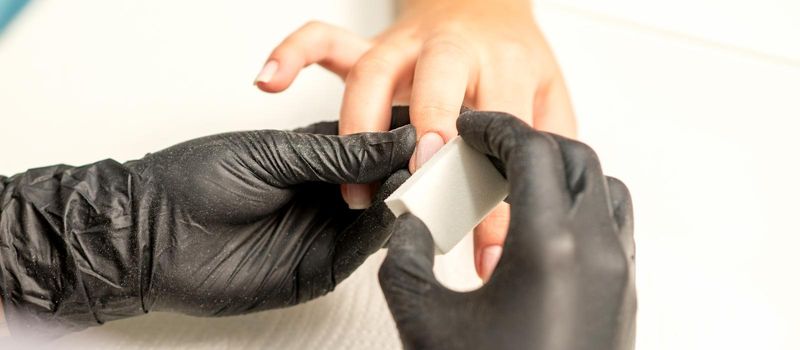 Close up of the caucasian hands of a professional manicurist are filing the nails of a young woman. Young caucasian woman receiving a manicure by a beautician with a nail file in a nail salon