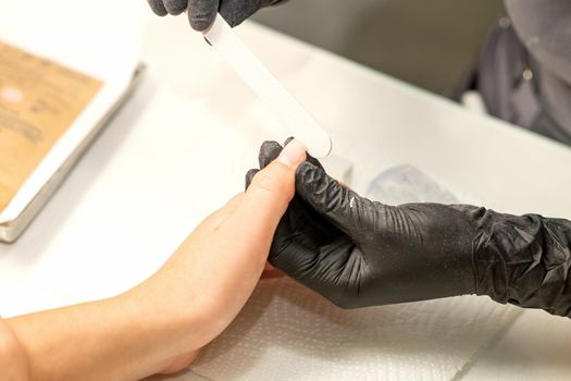 Close up of the caucasian hands of a professional manicurist are filing the nails of a young woman. Young caucasian woman receiving a manicure by a beautician with a nail file in a nail salon