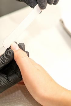 Close up of the caucasian hands of a professional manicurist are filing the nails of a young woman. Young caucasian woman receiving a manicure by a beautician with a nail file in a nail salon