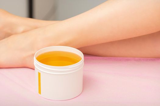 Woman legs with a white jar of wax sugaring before hair removal at the spa