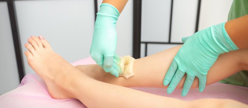 Waxing depilation procedure for removing hair on legs with sugaring paste in the beauty salon
