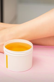 Woman legs with a white jar of wax sugaring before hair removal at the spa