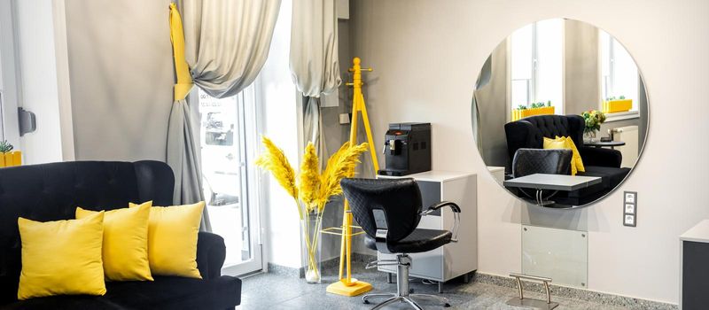 Modern small bright hair and beauty salon in black and yellow colors with gray walls and floor and black sofa with yellow cushions