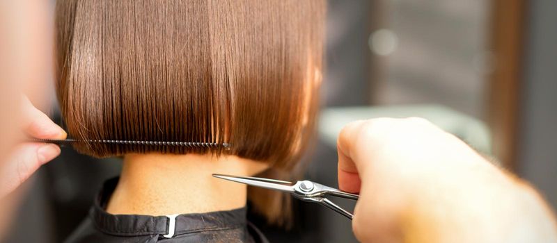 Haircut of short hair of young white woman by hands of a hairdresser in a hair salon, back view, close up