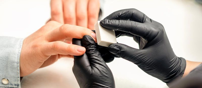 Close up of the caucasian hands of a professional manicurist are filing the nails of a young woman. Young caucasian woman receiving a manicure by a beautician with a nail file in a nail salon