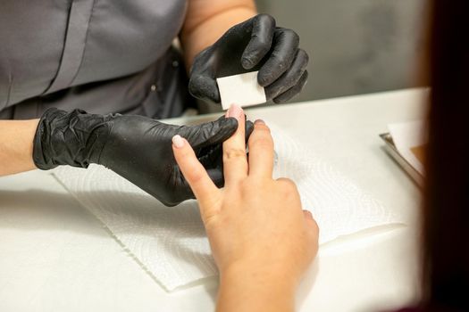 Close up of the caucasian hands of a professional manicurist are filing the nails of a young woman. Young caucasian woman receiving a manicure by a beautician with a nail file in a nail salon