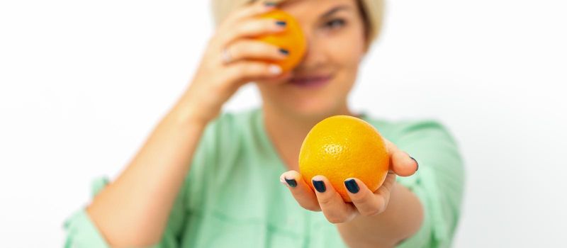 Smiling female nutritionist holding a whole orange, offering and looking at camera over white background, healthy diet concept