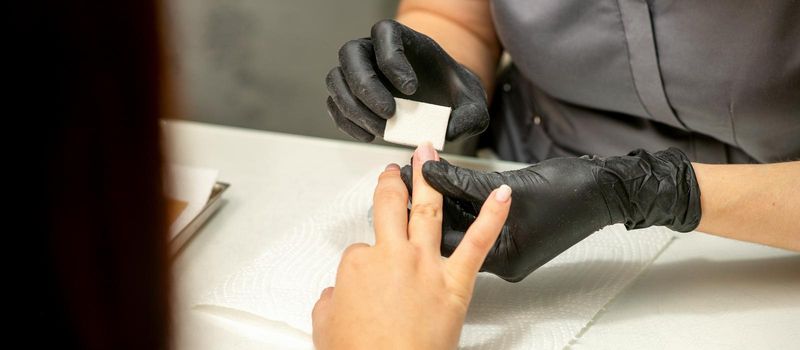 Close up of the caucasian hands of a professional manicurist are filing the nails of a young woman. Young caucasian woman receiving a manicure by a beautician with a nail file in a nail salon